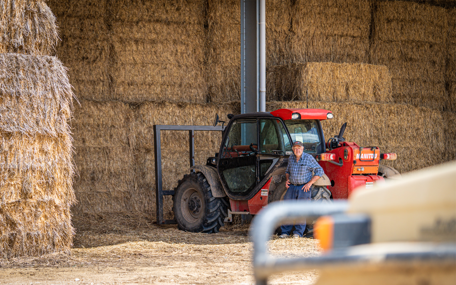 A farmer standing in front of a red tractor, and a hot dip galvanised hay shed in Victoria, Australia.