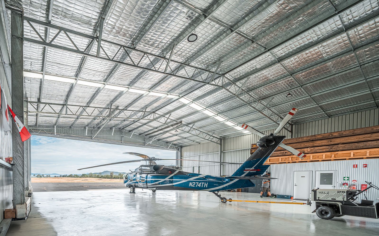 A parked Black Hawk helicopter in an aircraft hangar, attached to an airstrip tow vehicle with a built-in office in the background.