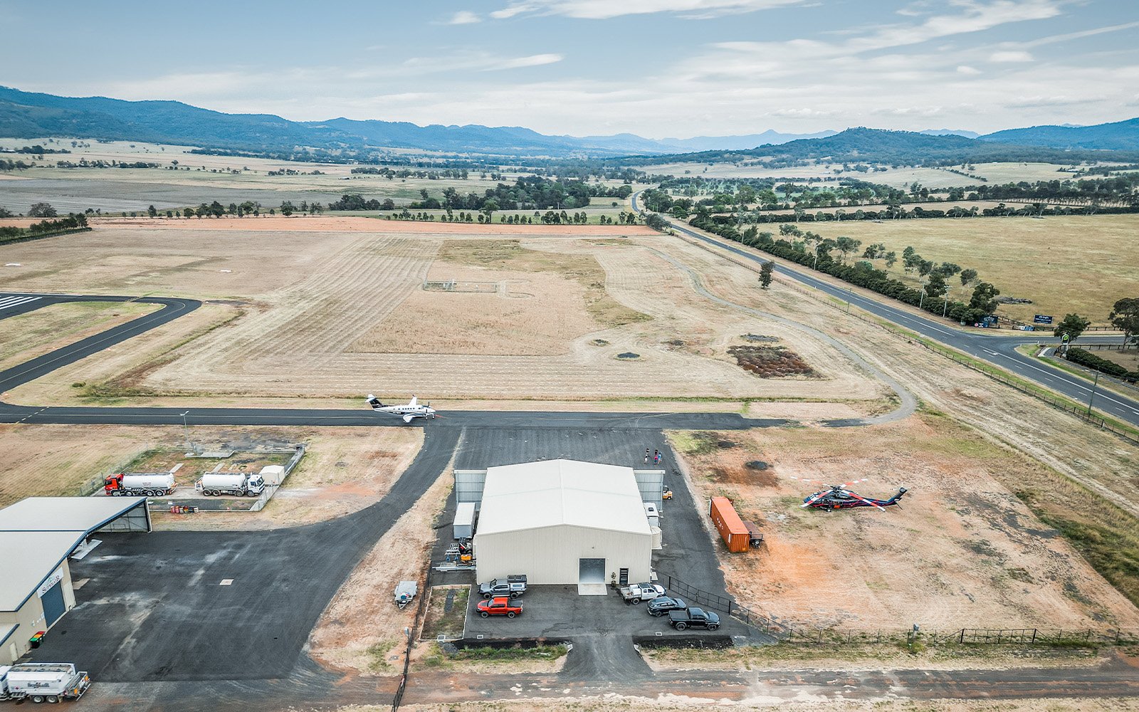 A helicopter hangar in the Hunter Valley, NSW, seen from above, with an emergency services Black Hawk to its right, a prop plane on the tarmac, and another hangar to its left.